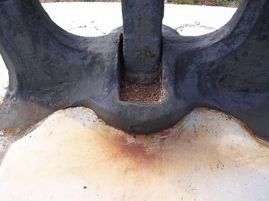 Corrosion of a ship's anchor and staining of its concrete base.