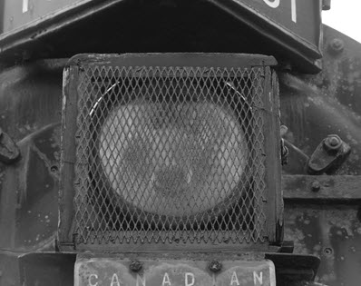 The headlight of a steam locomotive located outdoors is protected by steel screening.