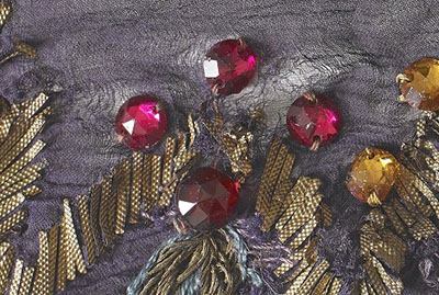 Delicate crepe fabric has become distorted and torn around red faceted cut glass faux jewels.