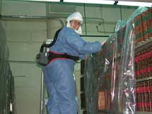 Person wearing Personal Protective Equipment and covering books and shelves in a plastic sheeting to prevent the spread of spores.