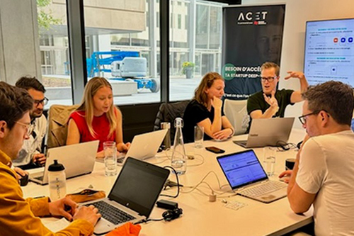 The photo shows a co-development workshop for entrepreneurs at ACET. Seven people are sitting around a conference table and discussing amongst themselves.