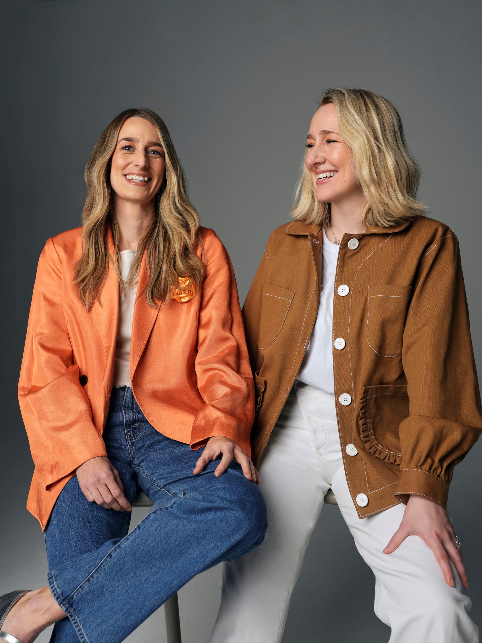 Romy et Myriam Belzile-Maguire, fondatrices de la marque de chaussures Maguire. tout sourire, assises sur un tabouret.
