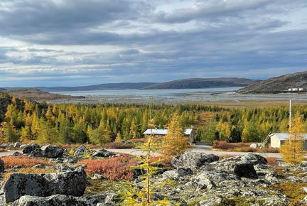 Boreal forest in autumn, rocks in the foreground and a body of water on the horizon under a cloudy sky.