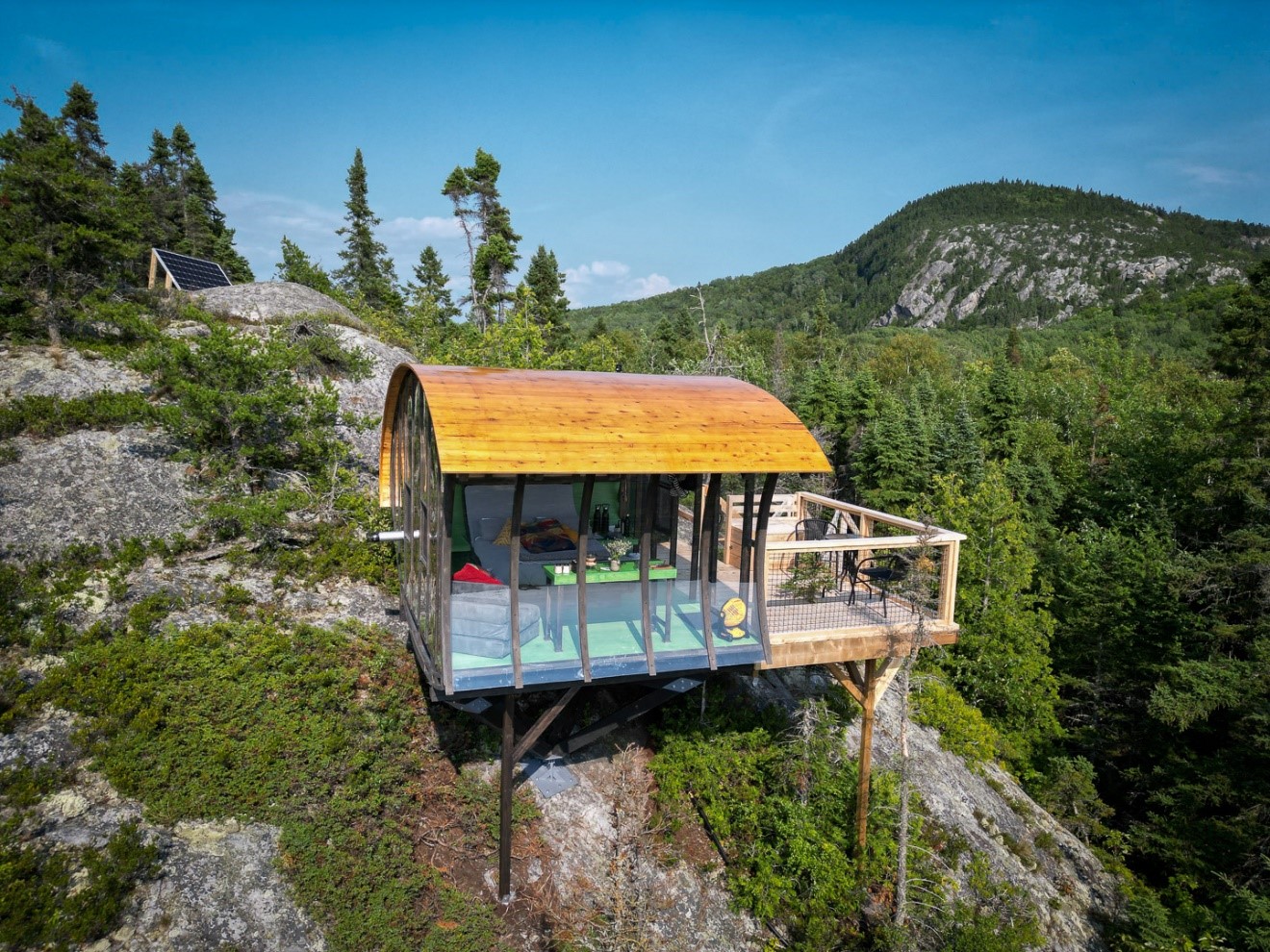 Photo de la cabine Ovum, aux Perchoirs du Cirque, perchée sur un escarpement rocheux, avec vue sur la forêt et les montagnes environnantes.