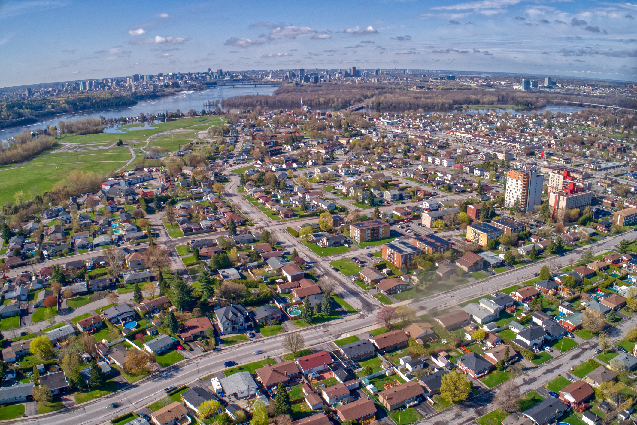 Vue aérienne d’un quartier résidentiel de Gatineau en bordure de la rivière des Outaouais, avec le centre-ville visible au loin.