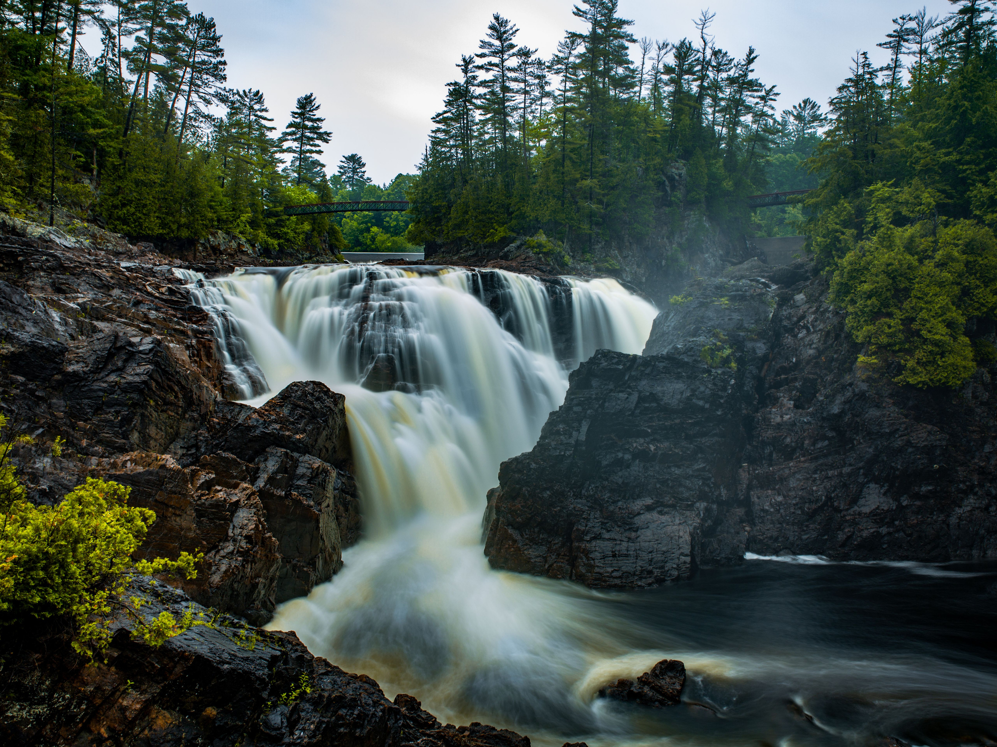 Waterfall surrounded by rocky cliffs and a conifer forest.