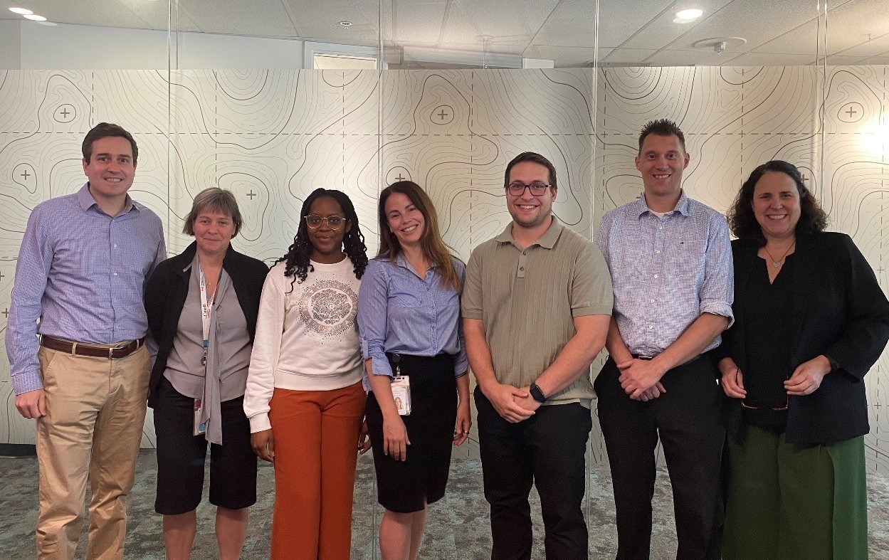 Seven members of the Outaouais Business Office team pose in a meeting room in front of a glass wall decorated with a topographic pattern.