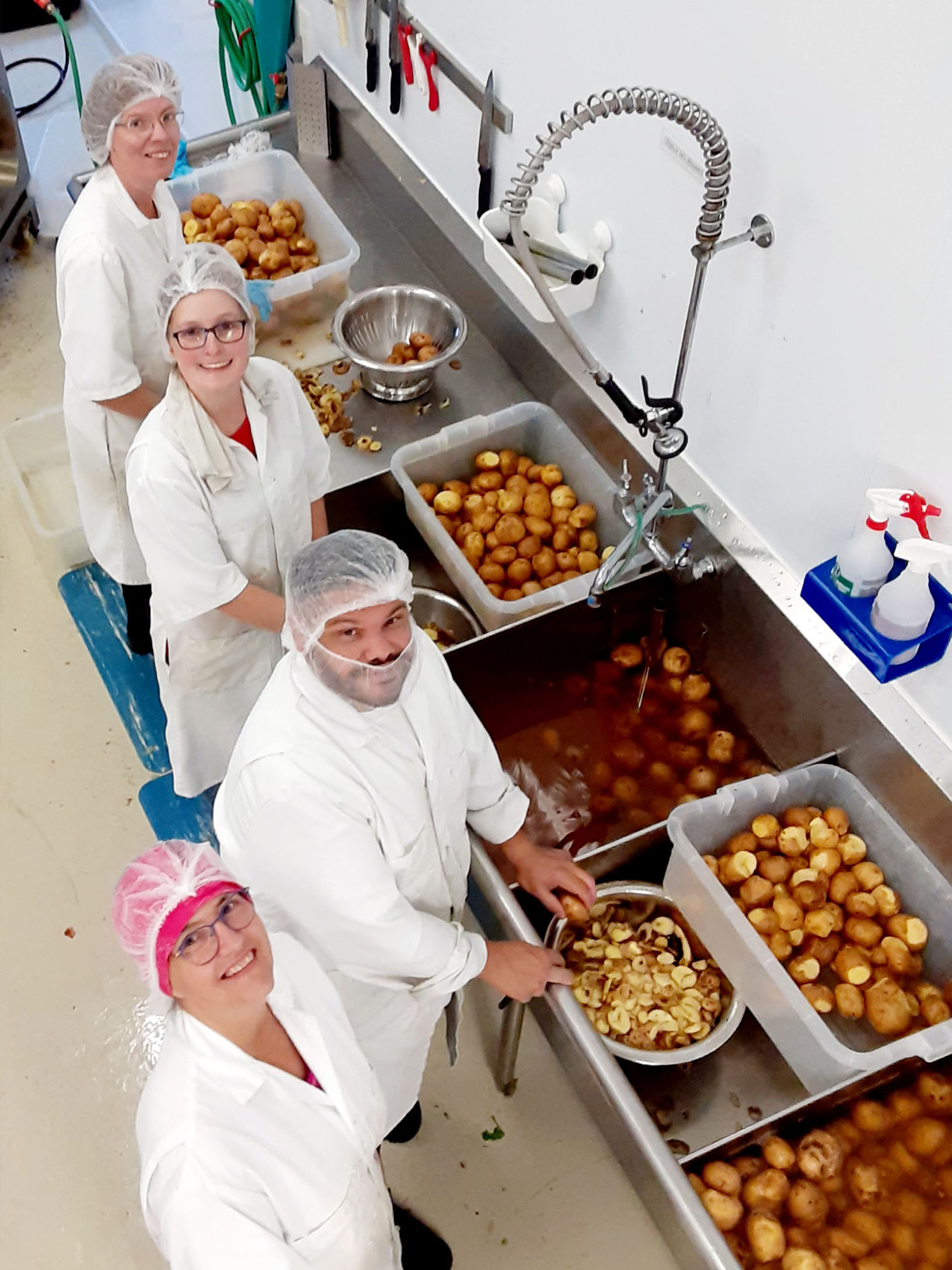 Employés nettoyant et épluchant des pommes de terre à un poste de lavage industriel.