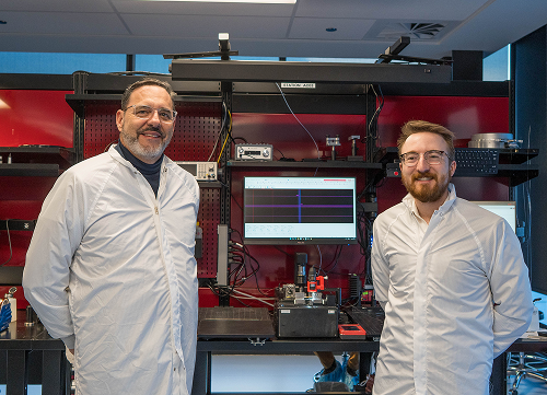 Photo taken during a visit to LumIR Lasers. Sony Perron, Deputy Minister and President of CED, and Philippe Bleau, President of LumIR Lasers, wearing lab coats in front of a technical workstation equipped with measuring instruments and a screen displaying graphics.