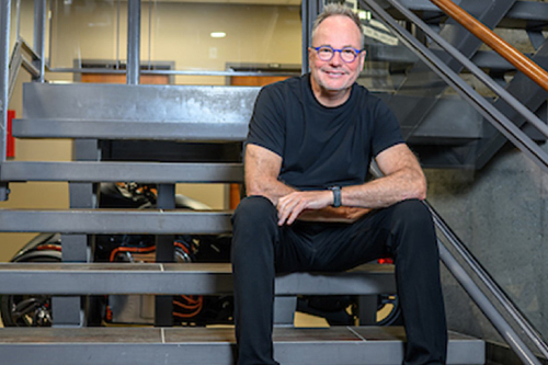 Photo de Ghyslain Goulet, président-directeur général de l’ACET, tout sourire, vêtu d’un jean et d’un t-shirt. Il est assis sur les marches d’un escalier à l’intérieur du siège social de l’organisation.