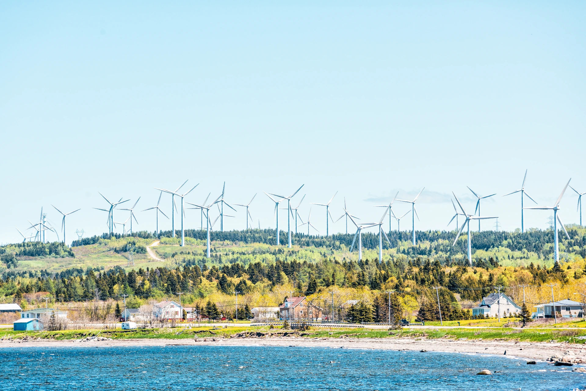 In Gaspésie, a coastal village in the foreground of the photo gives a glimpse of a large-scale wind farm in the background