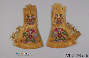 Photo of tan leather gloves, top view, featuring some decorative embroidery, with catalogue number VI-Z-76 a,b on a grey background.