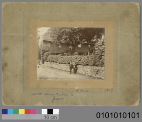 Black and white photo of two figures standing by a stone wall  framed with border and a 10 cm colour scale and the number 0101010101.