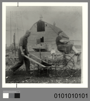 Black and white photo of a man using an agricultural tool in front of a barn with a grey scale and the number: 0101010101.