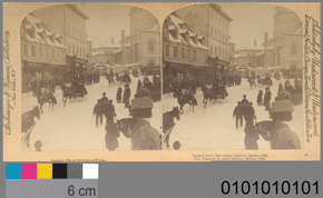 Black and white stereograph of a busy urban street in the winter with a 10cm scale and the number 0101010101