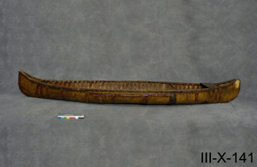 Final view of a wooden canoe with neutral grey background, with catalogue number III-X-141 on a grey background.