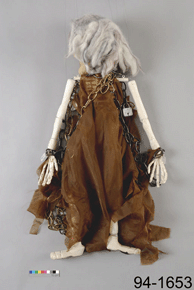 Reverse view of a doll with skeletal arms/lets in a loose brown dress with the number 94-1653