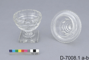 Colour image of intricate glass or crystal container with a lid by its side, includes 10cm colour scale and D-7008.1 a-b