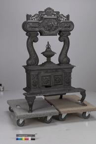 Colour photo of cast-iron stove with decorative mantle, situated on two wheeled platforms, with catalogue number A-1901 on a grey background.