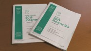 Photo of two paper 2019 income tax packages, with the package for Nunavut resting on top of the package for British Columbia