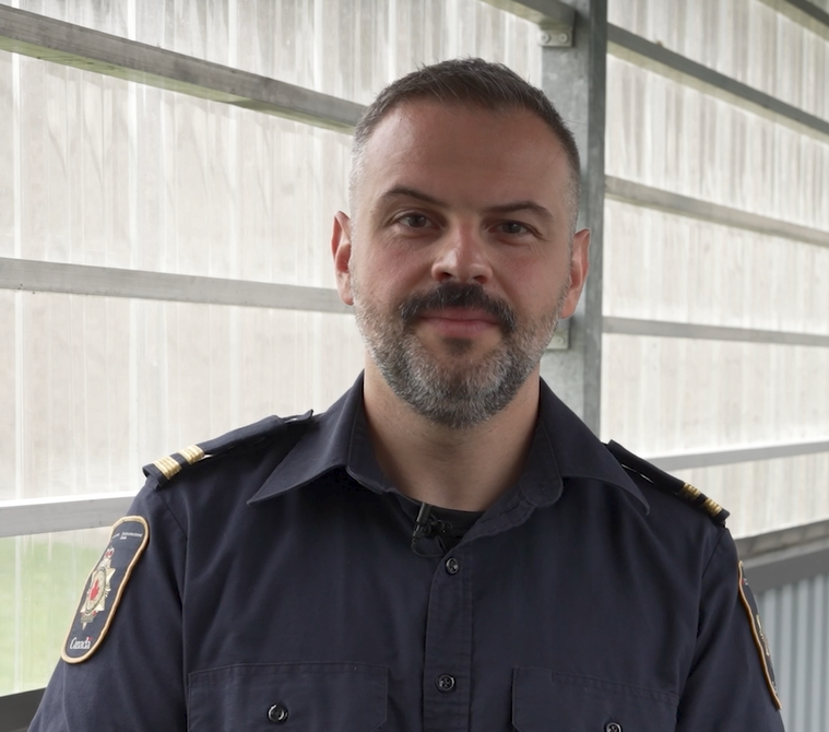 un homme avec des cheveux foncé et une barbe qui porte un uniforme d’agent correctionnel