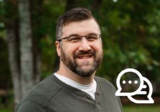 un homme portant des lunettes et un gilet gris sourit à la caméra