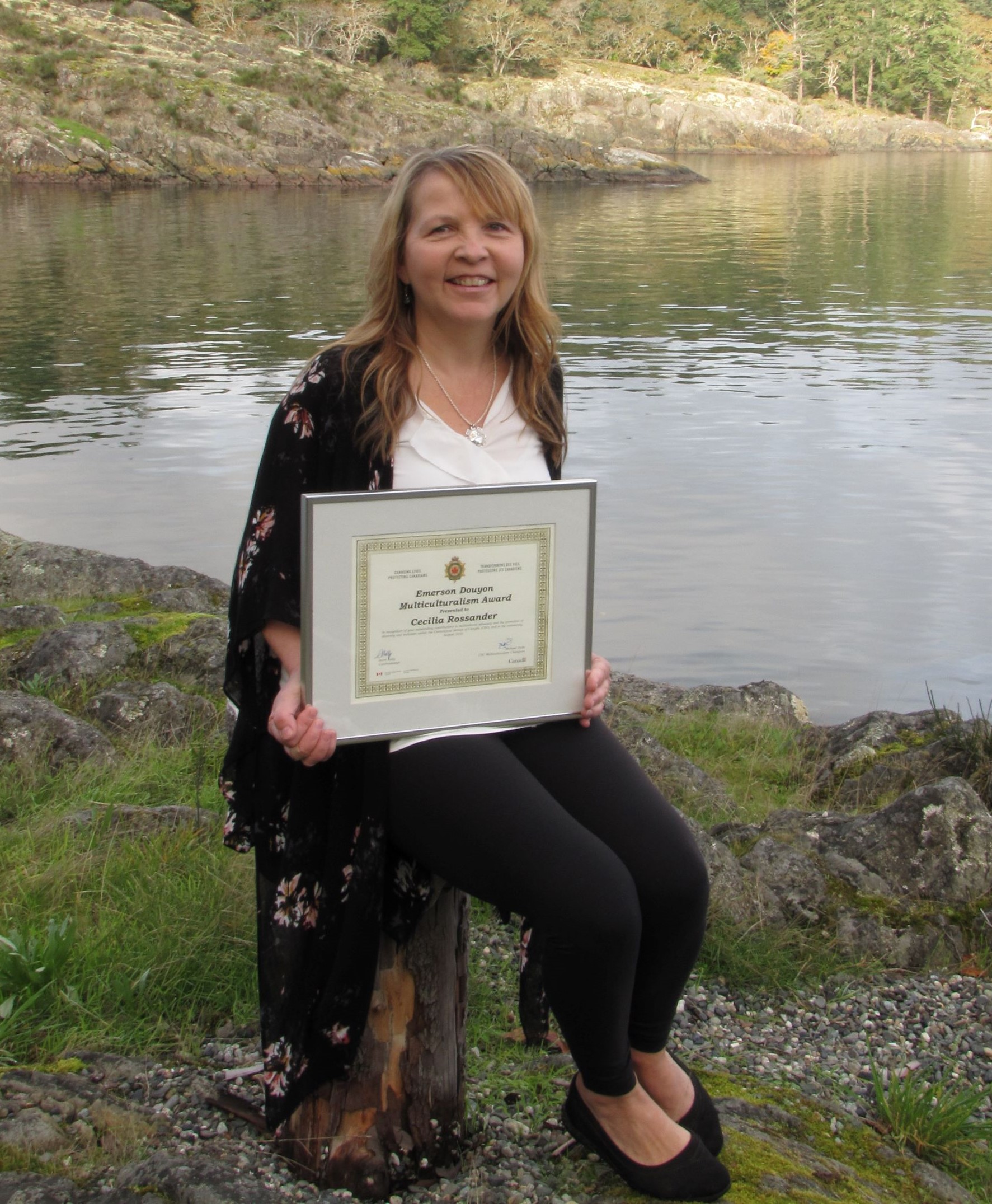 woman sitting on a stump holding a framed certificate