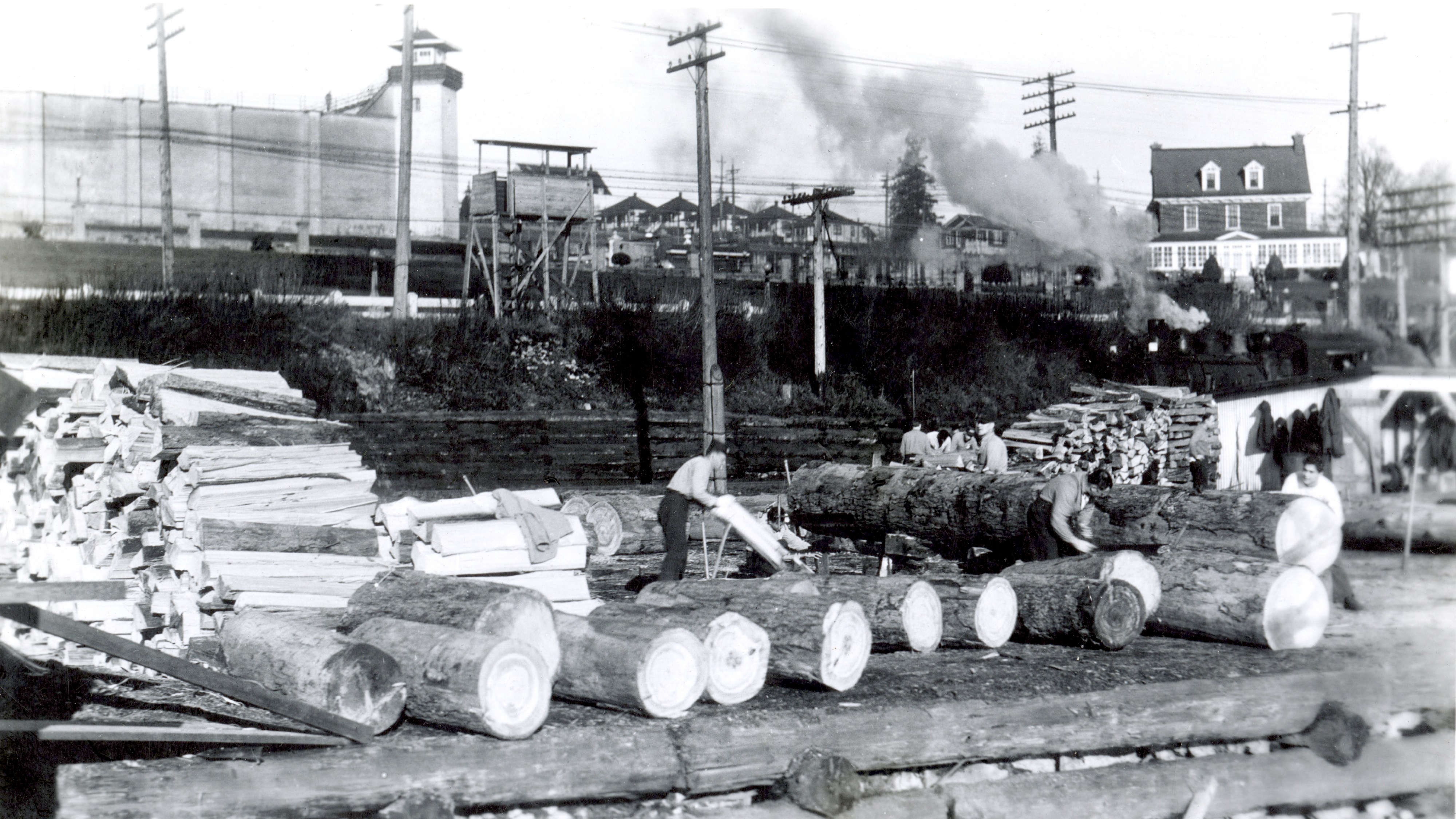 Logs piled on a dock with men sawing them