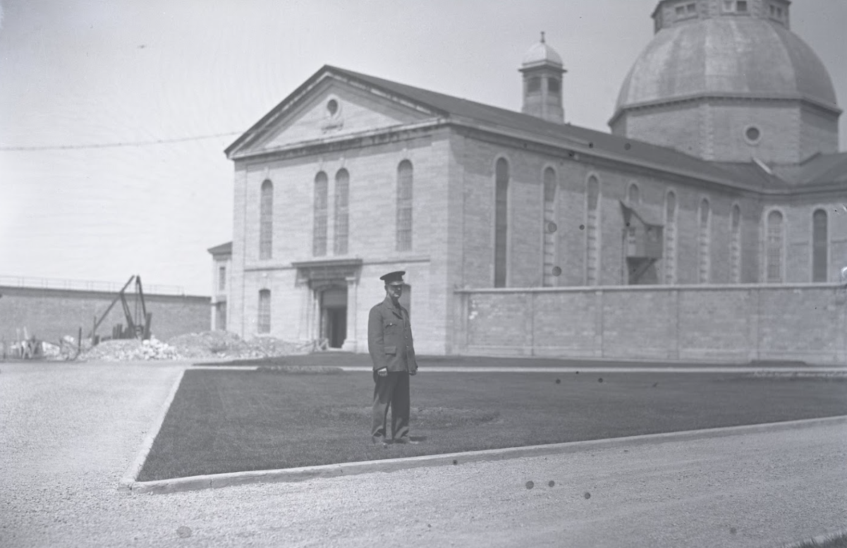 Aman in uniform stands outside stone building