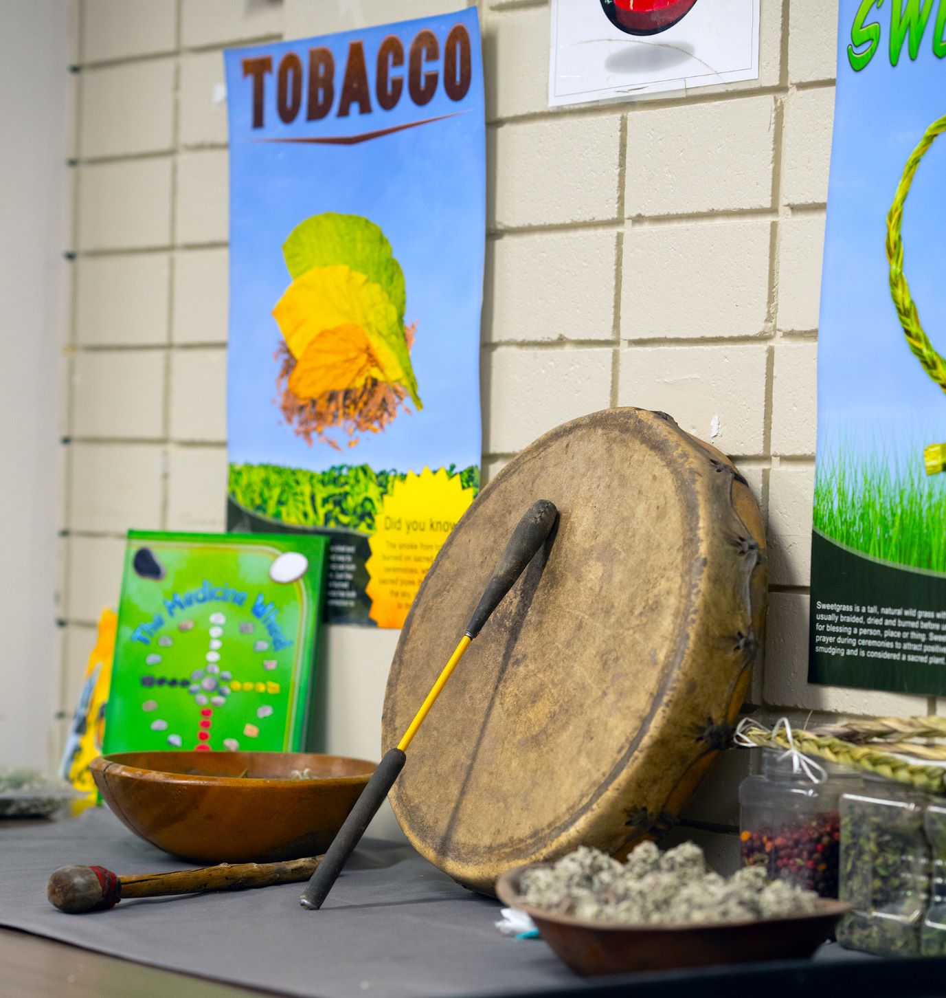 étagère sur laquelle sont rangés des objets culturels, un bol en bois, un tambour, une affiche au mur derrière avec la mention TOBACCO