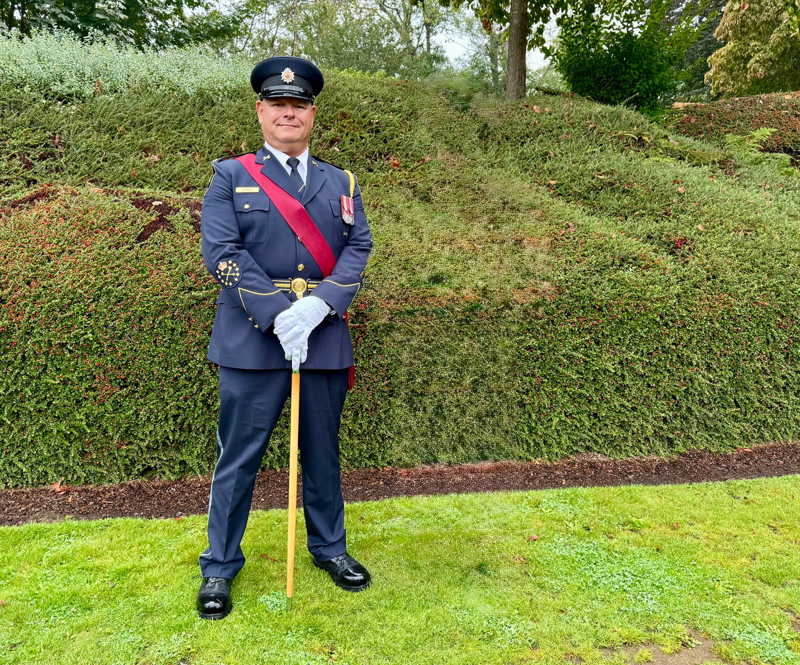 Uniformed CSC officer poses for photo in front of a hedge.