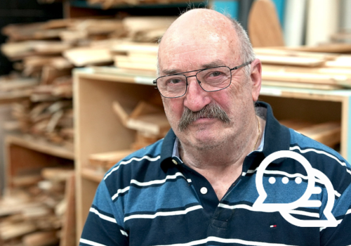A man wearing a blue striped shirt poses for a photo in front of a woodworking station