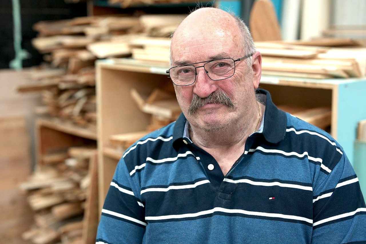 A man wearing a blue striped shirt poses for a photo in front of a woodworking station
