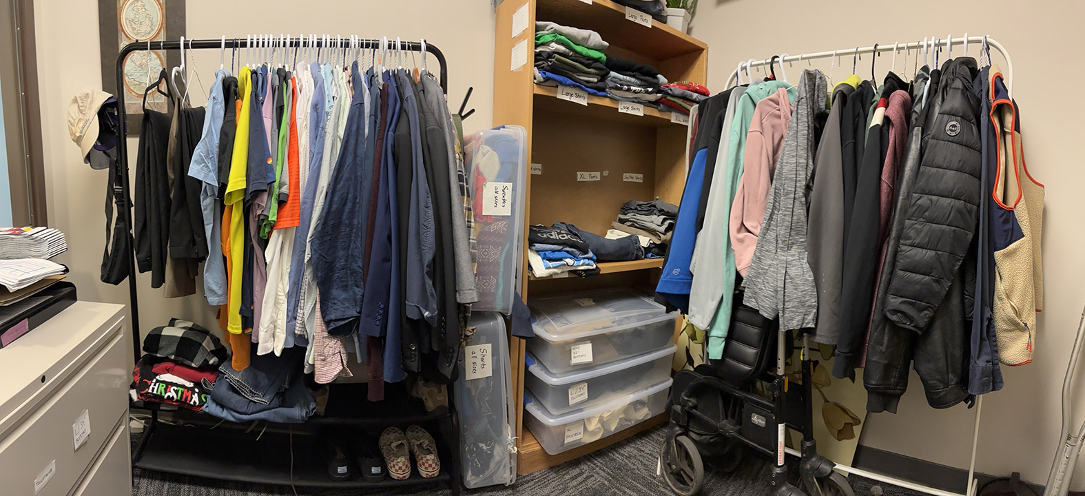Two racks of coats and shirts with a shelf with various clothing items and boxes in between.