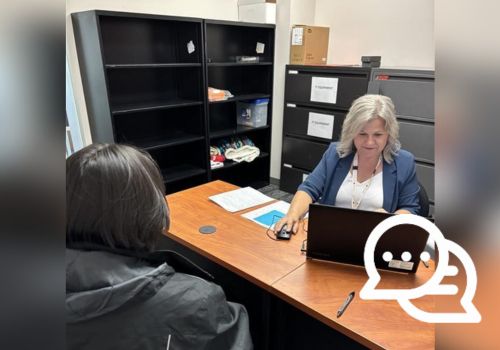 Une femme assise à un bureau travaille sur un ordinateur portatif pendant qu’un homme faisant dos à la caméra est assis devant elle.