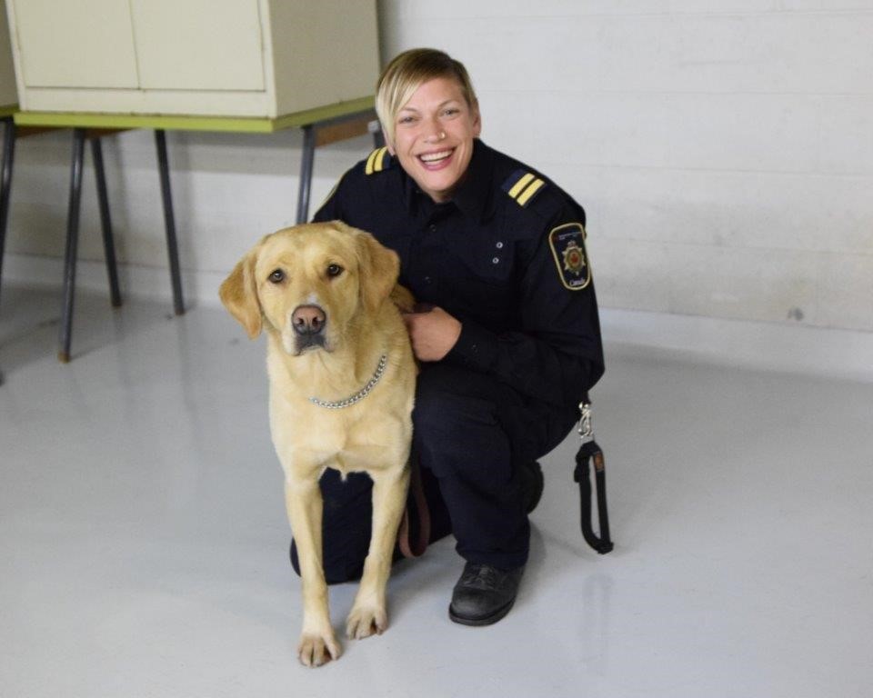 Dana Hackl porte un uniforme d’agente correctionnelle bleu foncé avec Robyn, un chien Golden Labrador (un mélange de Golden Retriever et de Labrador blond)