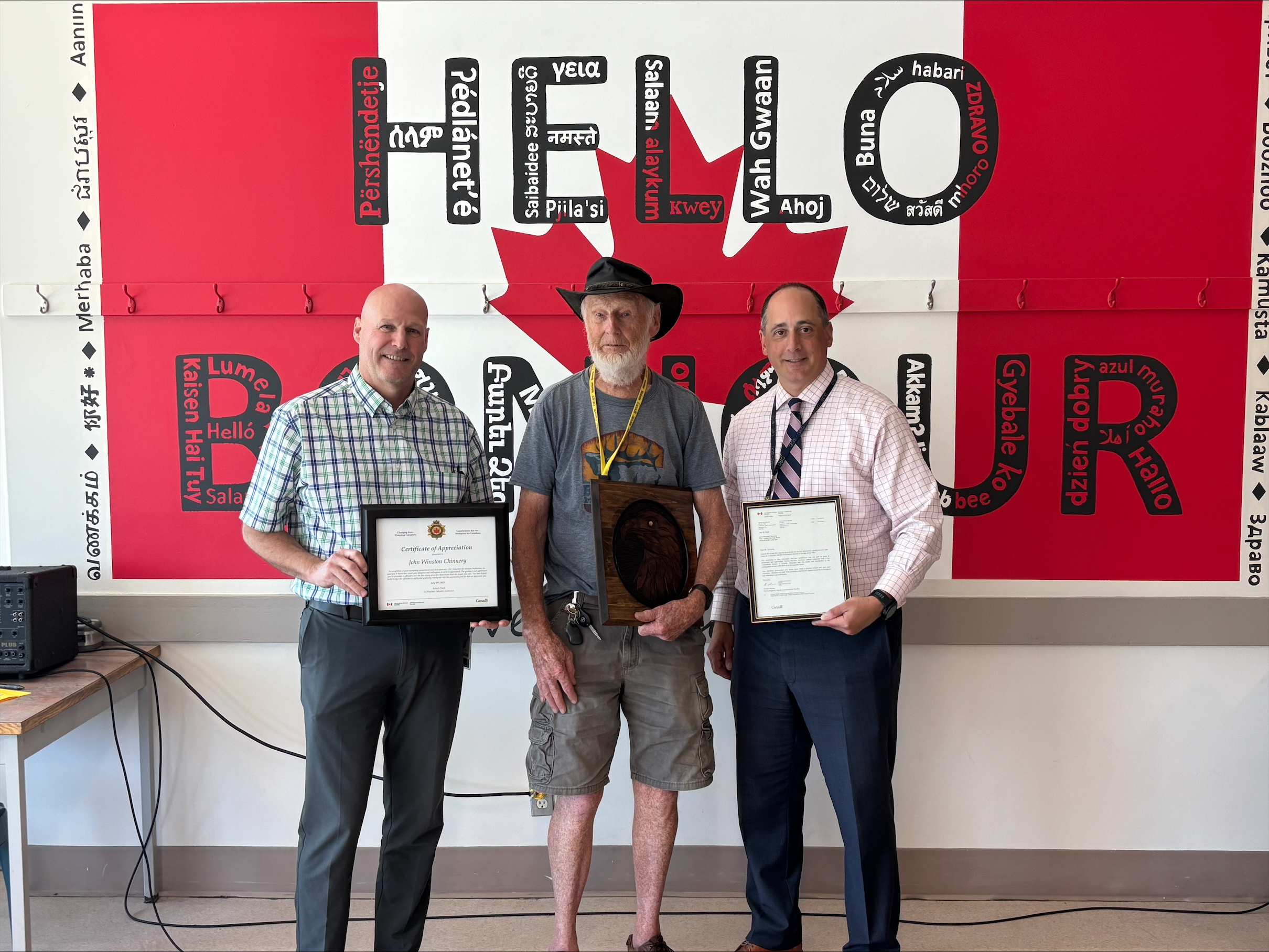 Three men are standing and smiling together. Each man is holding a plaque.