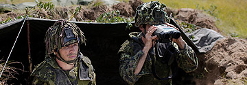 2 Soliders in a tent with one looking through binoculars.