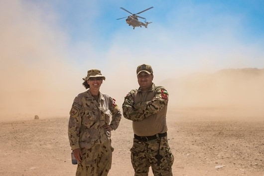 Le major Jillian Pare et le major jordanien Mohammad M. Brahmeh se tiennent devant un hélicoptère Super Puma de la Jordanie qui effectue un décollage au cours de l’exercice OLIVE GROVE, un exercice d’entraînement interarmées qui se déroule dans le désert, en Jordanie, dans le cadre de l’opération IMPACT, le 9 septembre 2019.