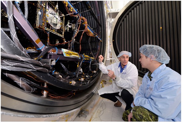 This photo shows two scientists in clean room garb going over the electronics of a satellite