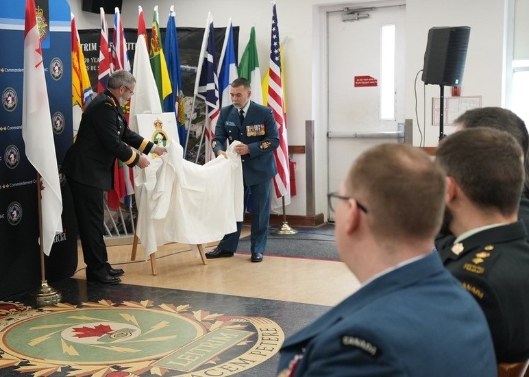 Two senior CAF members in uniform unveil the CAFCYBERCOM badge display, with flags and seated personnel in the room.