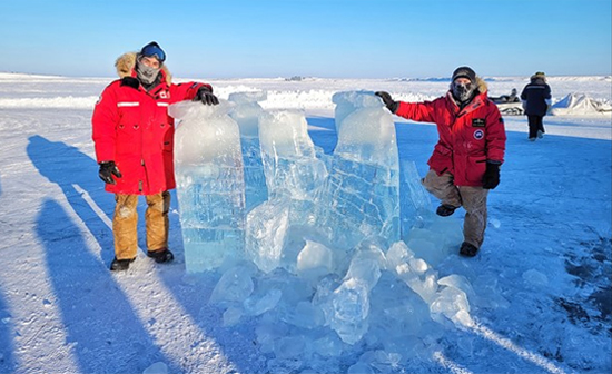 Two men stand next to large pieces of ice.