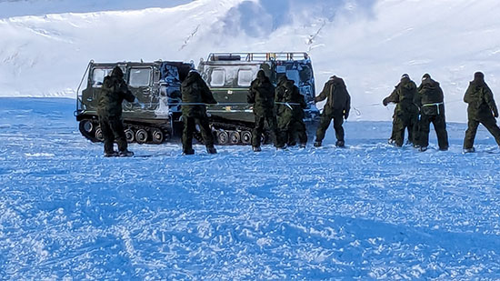 A group of Canadian Armed Forces members in front of a vehicle with tracked wheels on a snow-covered field.