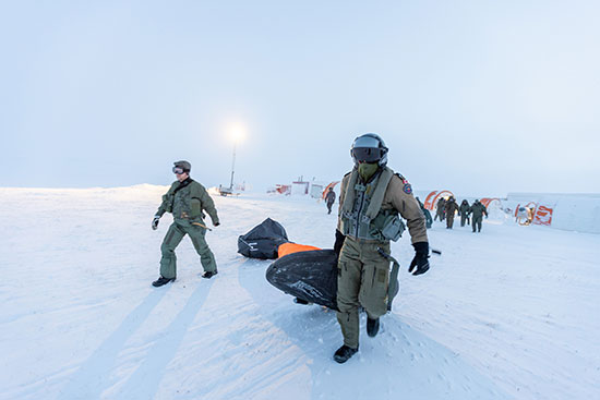 A Canadian Armed Forces pilot (right) and a Norweigan pilot (left) drag a survival kit across an Arctic plain.