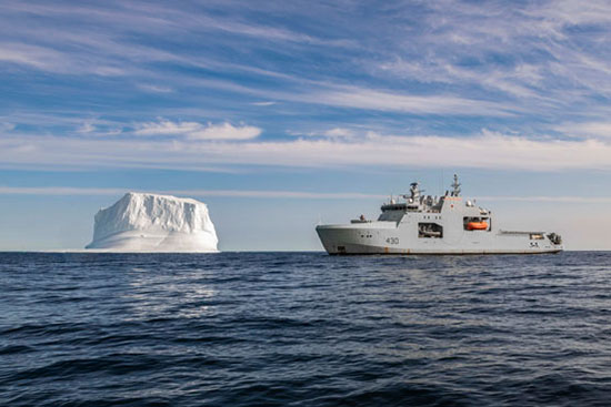 A grey Royal Canadian Navy vessel, the HMCS Harry DeWolf, is shown with an iceberg.