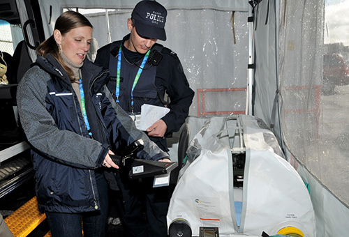 A women and a man look at a handheld radiation detector inside a white tent.