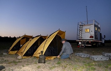 A person kneeling beside yellow tents at sunset