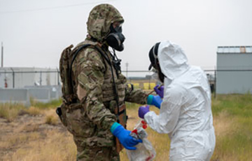 Soldier in camouflage protective gear being swabbed by staff member in white protective gear.