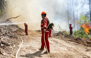 Des personnes en tenue de protection rouge arrosent le sol enfumé d’une forêt en feu.
