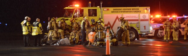 Un groupe de pompiers munis d’une tenue de protection se tiennent devant un véhicule du service des incendies de l’aéroport durant l’exercice de gestion des urgences de la Ville d’Ottawa.